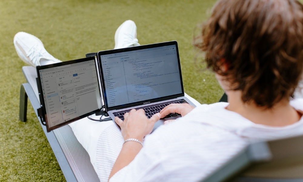 Persona trabajando desde el exterior durante las vacaciones con un notebook y monitor portátil Mobile Pixels, gestionando correos y tareas en doble pantalla para resolver trabajo rápido y volver a disfrutar el descanso.