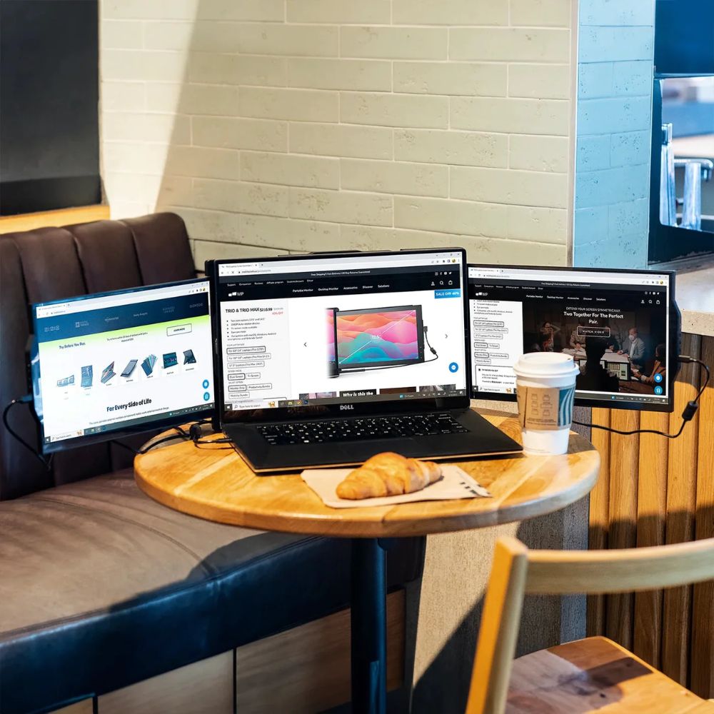 Persona utilizando monitor portátil Mobile Pixels Trio Max con laptop en un café; configuración de triple pantalla ideal para realizar múltiples tareas como correo, análisis de datos y navegación web en movimiento.