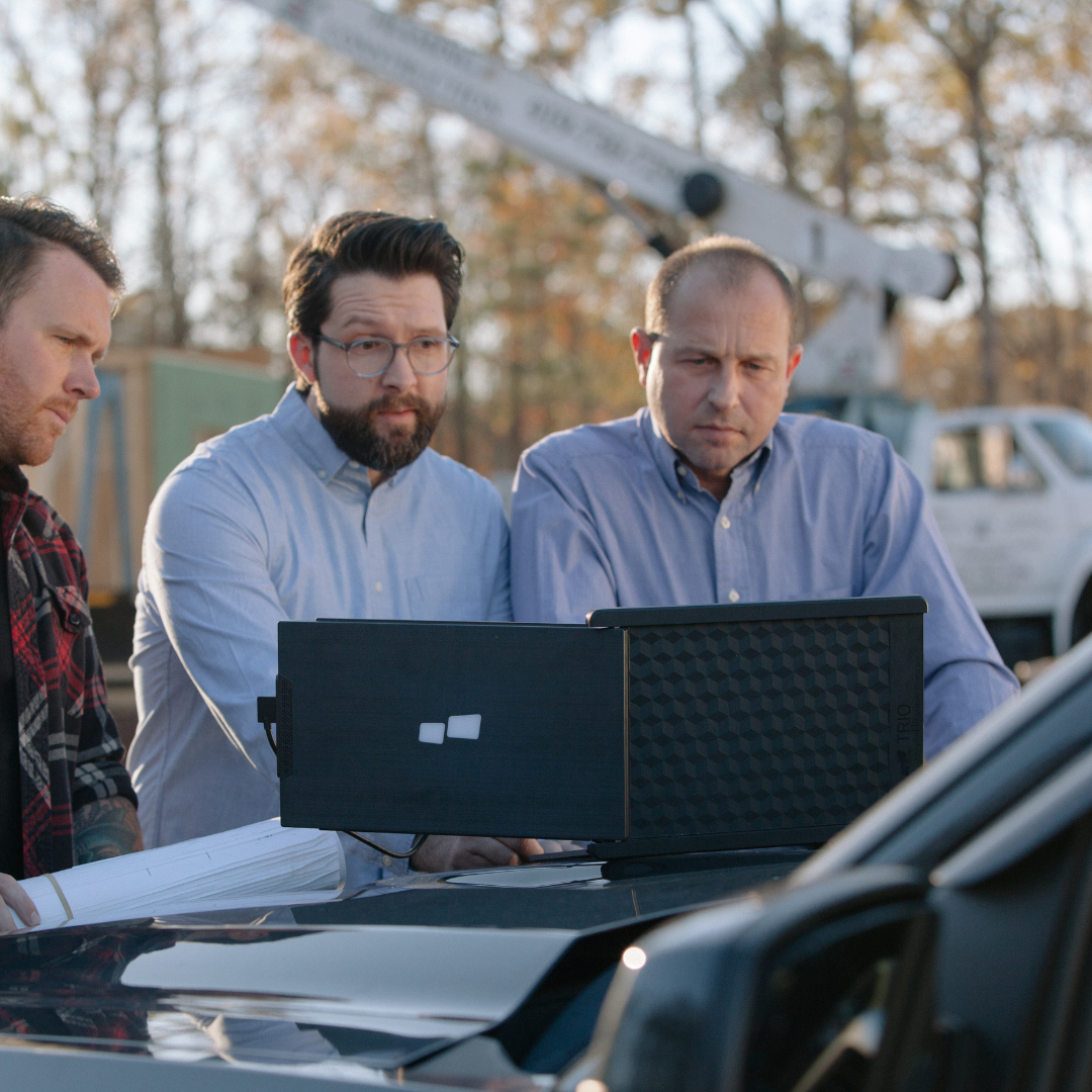 Equipo de trabajo revisando planos y datos en monitor portátil en terreno de construcción