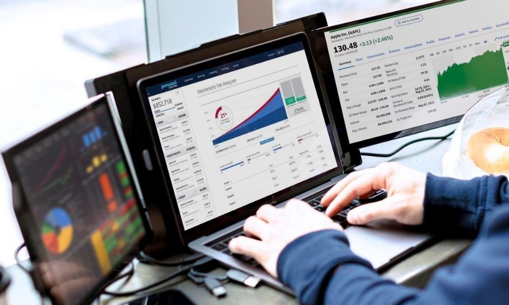 Persona trabajando en un laptop equipado con el monitor portátil Mobile Pixels Trio Max, mostrando múltiples pantallas con gráficos, análisis y paneles de productividad, ideal para trabajo remoto y multitarea profesional.