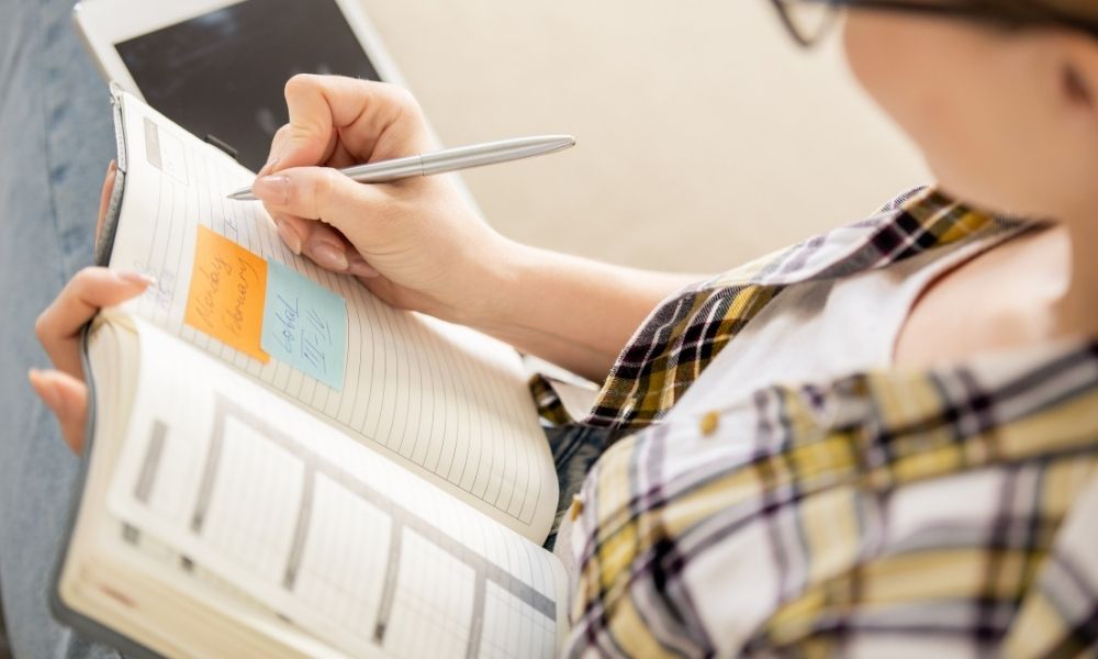 Persona planificando nuevas metas y objetivos del año en una agenda con notas adhesivas, representando organización, enfoque y productividad para alcanzar sueños y proyectos personales.