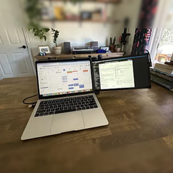 Cliente satisfecho utilizando monitor portátil Mobile Pixels como pantalla secundaria para Google Calendar y gestión de proyectos; estación de trabajo organizada desde casa con laptop y pantalla extendida.